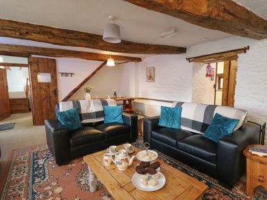 A living room with two black sofas a wooden coffee table with tea set and cakes and beams on the ceiling at Y Beudy in Cwmiar near Llanybydder