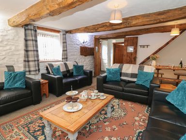 A living room with black leather sofas and blue cushions around a wooden coffee table with tea set and snacks at Y Beudy in Cwmiar near Llanybydder