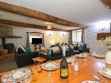 A living room with wooden beams a dining table set with plates glasses and cutlery and leather sofas at Y Beudy in Cwmiar near Llanybydder