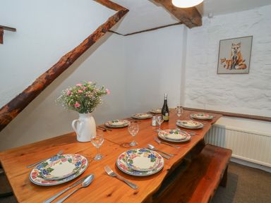 A wooden dining table set with plates glasses cutlery and flowers in a white jug at Y Beudy in Cwmiar near Llanybydder