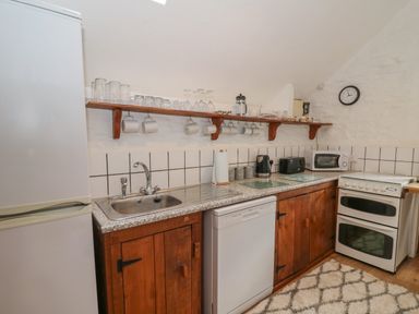 A kitchen with a refrigerator sink dishwasher oven microwave and wooden cabinets at Y Beudy in Cwmiar near Llanybydder