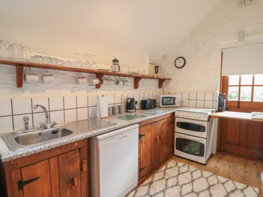 A kitchen with wooden cabinets a sink dishwasher oven microwave and utensils at Y Beudy in Cwmiar near Llanybydder