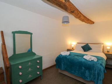 A bedroom with a bed with teal blanket and pillows two nightstands with lamps and a green dresser with mirror at Y Beudy in Cwmiar near Llanybydder
