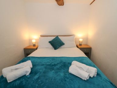 A bedroom with a double bed with teal blanket and pillow and bedside tables with lamps at Y Beudy in Cwmiar near Llanybydder