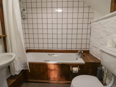 A bathroom with a bathtub surrounded by wood paneling a white tiled wall a toilet and a sink at Y Beudy Cwmiar near Llanybydder