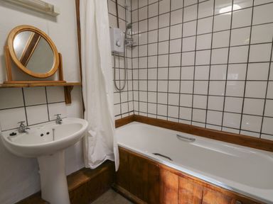 A bathroom with a bathtub wooden paneling white tiled wall a sink and a mirror at Y Beudy Cwmiar near Llanybydder