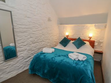 A bedroom with a double bed with teal blankets and pillows beside a white stone wall at Y Beudy in Cwmiar near Llanybydder