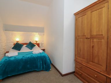 A bedroom with a double bed with blue pillows and blanket and a wooden wardrobe at Y Beudy in Cwmiar near Llanybydder