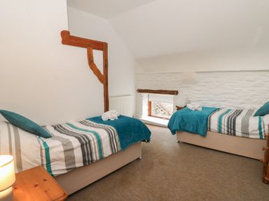 A bedroom with two single beds and a small window at Y Beudy in Cwmiar near Llanybydder
