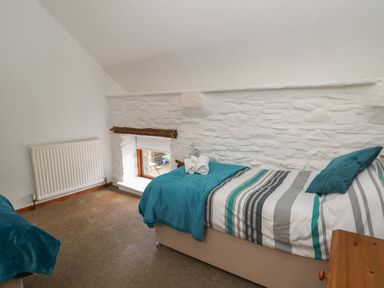 A bedroom with a single bed striped bedding a blue throw and pillows a small window and a radiator at Y Beudy Cwmiar near Llanybydder