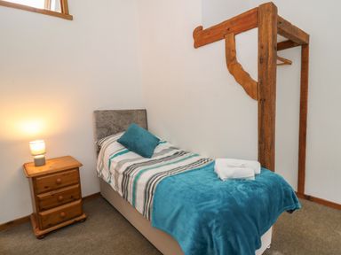 A bedroom with a single bed bedside table lamp and wooden coat rack at Y Beudy in Cwmiar near Llanybydder