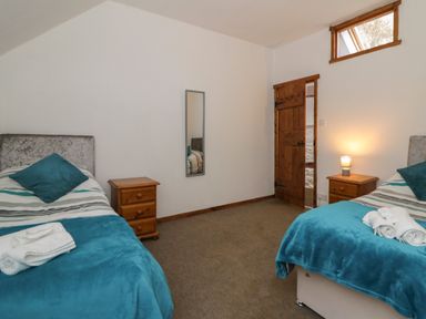A bedroom with two single beds bedside tables and a wooden door at Y Beudy in Cwmiar near Llanybydder
