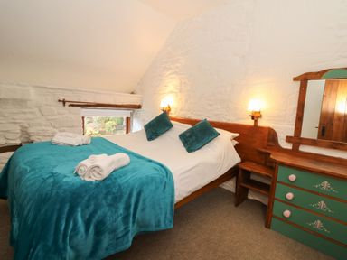 A bedroom with a double bed green pillows green blanket and a wooden dresser with mirror at Y Beudy in Cwmiar near Llanybydder