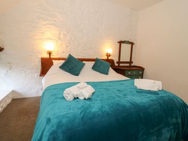 A bedroom with a double bed teal blanket and pillows bedside table with mirror and wall lights at Y Beudy in Cwmiar near Llanybydder