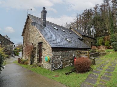 A stone cottage with a slate roof and small windows surrounded by grass and a paved path at Y Beudy in Cwmiar near Llanybydder