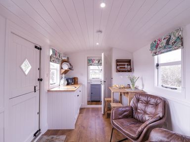 A kitchen and dining area with wooden countertops stools a small table brown leather chairs and windows with floral blinds at Bumbles Retreat in Whepstead near Bury St Edmunds
