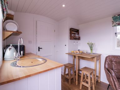 A small kitchen area with a wooden countertop sink kettle and toaster next to a wooden table with stools a vase with flowers and breakfast items at Bumble's Retreat in Whepstead near Bury St Edmunds