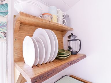 A kitchen shelf with white plates green bowls mugs a glass jar and a French press at Bumbles Retreat in Whepstead near Bury St Edmunds