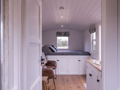 A small bedroom with a bed on a raised platform with storage cabinets underneath a window and a chair beside it at Bumbles Retreat in Whepstead near Bury St Edmunds