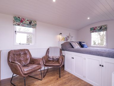 A bedroom with two brown chairs and a bed with storage underneath at Bumble's Retreat in Whepstead near Bury St Edmunds