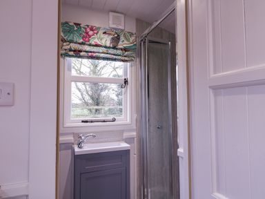 A small bathroom with a sink cabinet under a window and a glass shower door at Bumbles Retreat in Whepstead near Bury St Edmunds
