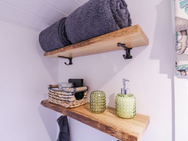 Wooden shelves with rolled towels a basket and soap dispenser in a bathroom at Bumbles Retreat in Whepstead near Bury St Edmunds