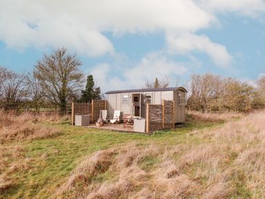 A small cabin with outdoor chairs and woven privacy screens in a grassy field at Bumbles Retreat in Whepstead near Bury St Edmunds