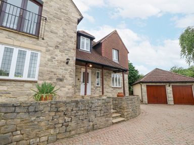 Exterior of a stone house with a paved driveway and a double garage with wooden doors at Sunningdale Rise in Preston