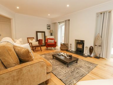A living room with a brown sofa a red armchair a wooden coffee table a decorative rug a fireplace and a large standing mirror at Sunningdale Rise in Preston