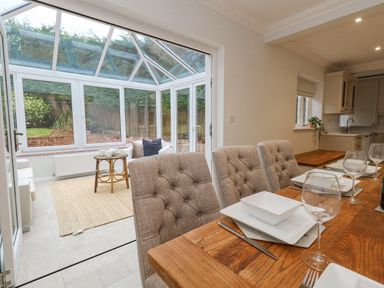 A dining area with a wooden table set with plates and glasses next to a conservatory with seating and a small table at Sunningdale Rise in Preston