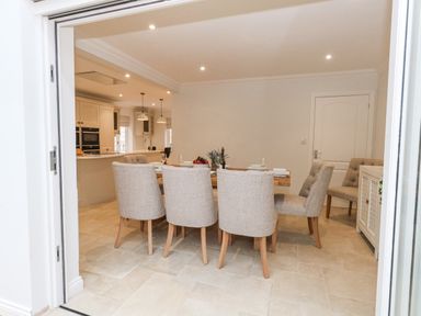 A dining area with a wooden table and six beige upholstered chairs next to a kitchen at Sunningdale Rise in Preston