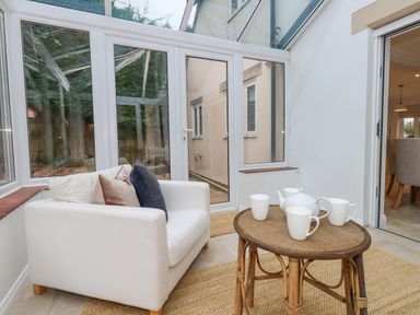 A conservatory with a white armchair with cushions and a wicker table with a teapot and cups at Sunningdale Rise in Preston