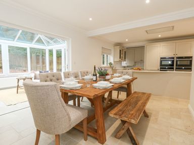 A dining area with wooden table set with dishes chairs and a bench next to a kitchen with white cabinets and double ovens at Sunningdale Rise in Preston