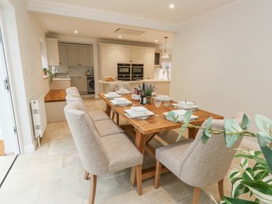 A dining area with a wooden table set for six and modern kitchen in the background at Sunningdale Rise in Preston