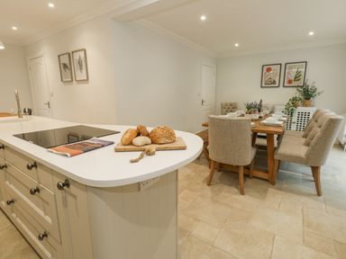 A kitchen island with bread and a book next to a dining table with six chairs and plants on it at Sunningdale Rise in Preston