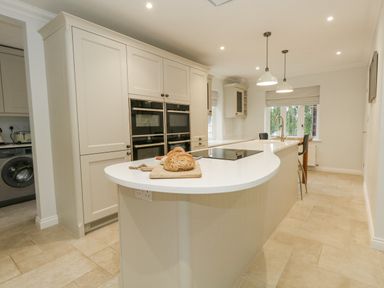 A kitchen with a curved island countertop with bread on a cutting board and double ovens built into cabinets at Sunningdale Rise in Preston