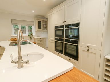 A kitchen with a white island countertop with a built-in sink and faucet ovens built into white cabinets at Sunningdale Rise in Preston