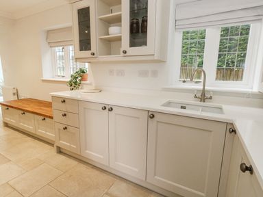 A kitchen with white cabinets a sink below window and a wooden bench at Sunningdale Rise in Preston