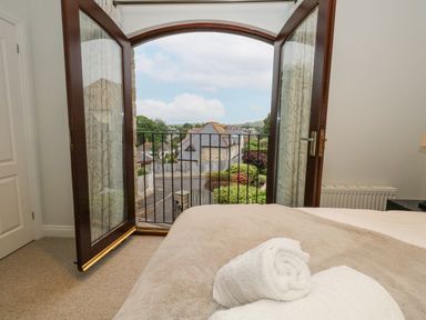 A bedroom with an open double door leading to a balcony overlooking houses and greenery at Sunningdale Rise in Preston