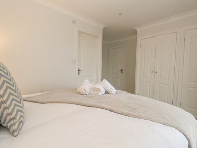 A bedroom with a bed, three rolled towels on the bed, two doors, and a double-door wardrobe at Sunningdale Rise in Preston