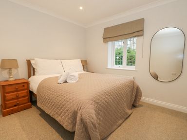 A bedroom with a bed covered with a brown quilt and white pillows two bedside tables with lamps a window with a beige blind and an oval mirror on the wall at Sunningdale Rise in Preston