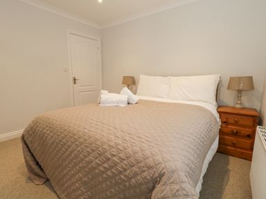 A bedroom with a bed covered by a quilted blanket with folded towels on it and wooden bedside tables with lamps at Sunningdale Rise in Preston