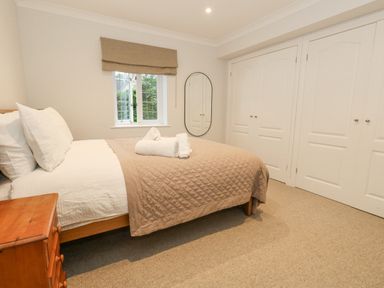 A bedroom with a bed linens and towels on it a wooden bedside table a window with blinds an oval mirror and built in wardrobes at Sunningdale Rise in Preston