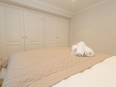 A bedroom with a bed covered by a beige quilt and rolled white towels on top in front of white double-door closets at Sunningdale Rise in Preston