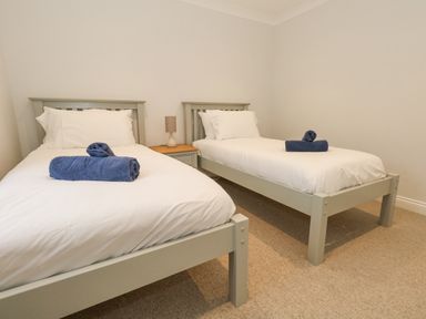 A bedroom with two single beds each with white bedding and blue towels on them separated by a nightstand with a lamp at Sunningdale Rise in Preston