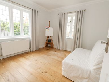A room with wooden floor two windows with curtains a white covered sofa and an easel with a small table at Sunningdale Rise in Preston