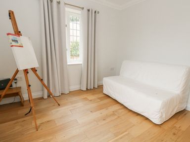 A room with a white sofa, an easel with a blank canvas, wooden floor, window with curtains at Sunningdale Rise in Preston