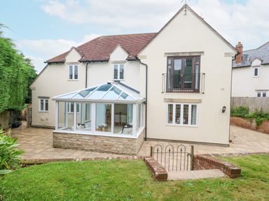 An exterior view of a two-story house with a glass conservatory patio doors and paved patio at Sunningdale Rise in Preston