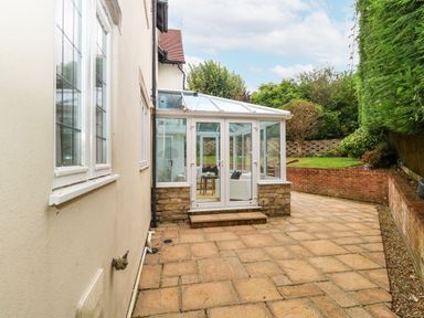A paved patio area with a glass conservatory attached to a house and a garden with bushes and a small tree at Sunningdale Rise in Preston