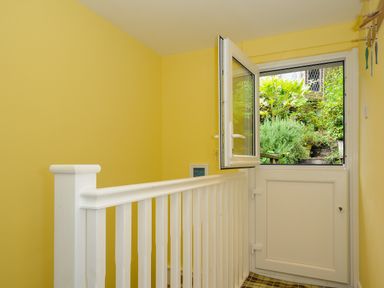A yellow hallway with a white railing and a half door opening to a garden at 15 The Moors in Lostwithiel